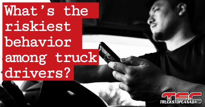 A professional truck driver operating a semi-truck while holding a cell phone, illustrating the rise in risky driving behaviors among truckers.