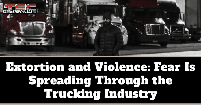 Extorsion news trucking Black-and-white image of a man wearing a winter coat and beanie standing in front of several parked semi-trucks at night, with the TruckStopCanada logo at the top. Text on the image reads: “Extortion and Violence: Fear Is Spreading Through the Trucking Industry.”