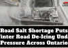 Road Salt Shortage Puts Winter Road De-Icing Under Pressure Across Ontario Snowplow operating on an icy highway, illustrating the road salt shortage and the pressure on winter road de-icing across Ontario. Text on graphic : Road Salt Shortage Puts Winter Road De-Icing Under Pressure Across Ontario